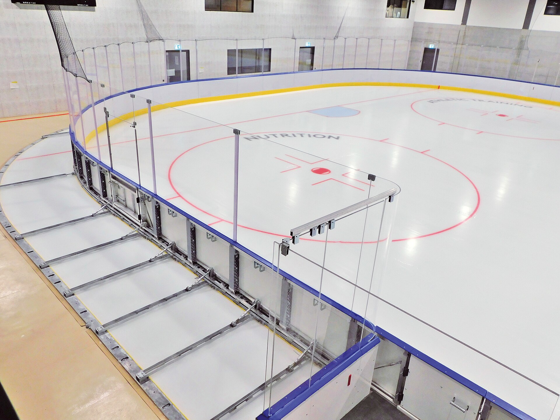 The empty ice surface of a community hockey arena, boards and benches around the rink